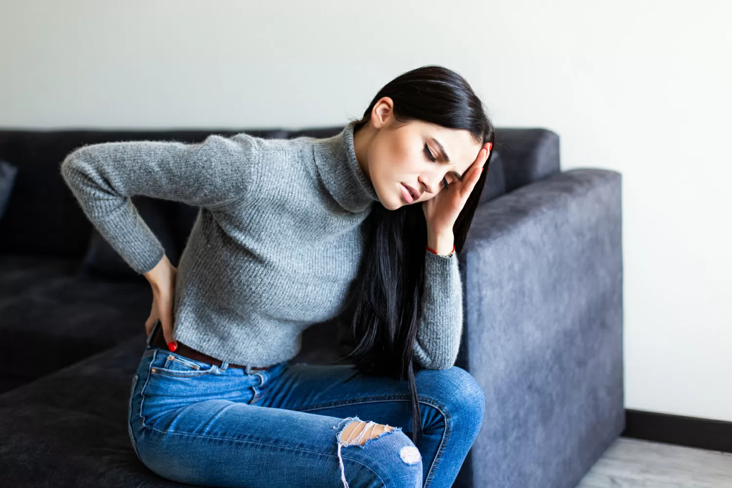 Young woman suffering back ache complaining sitting couch living room home